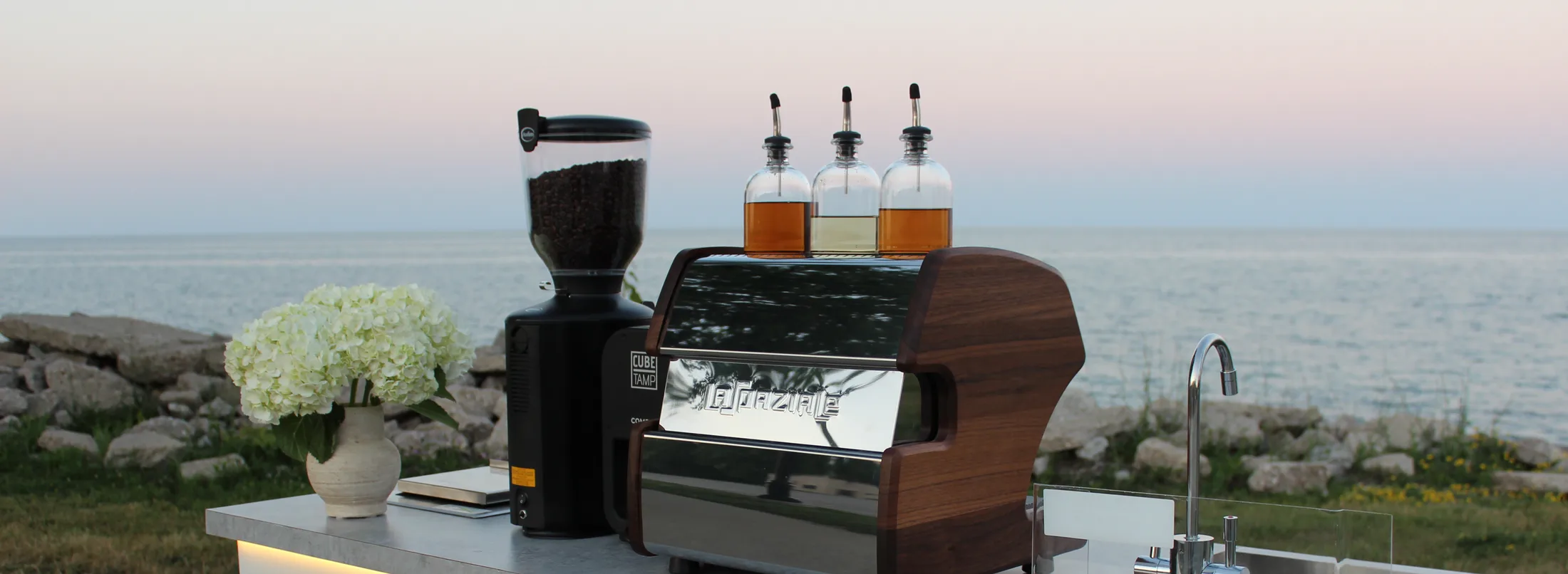White hydrangeas, grinder and espresso machine on the cart counter beside Lake Michigan at dusk