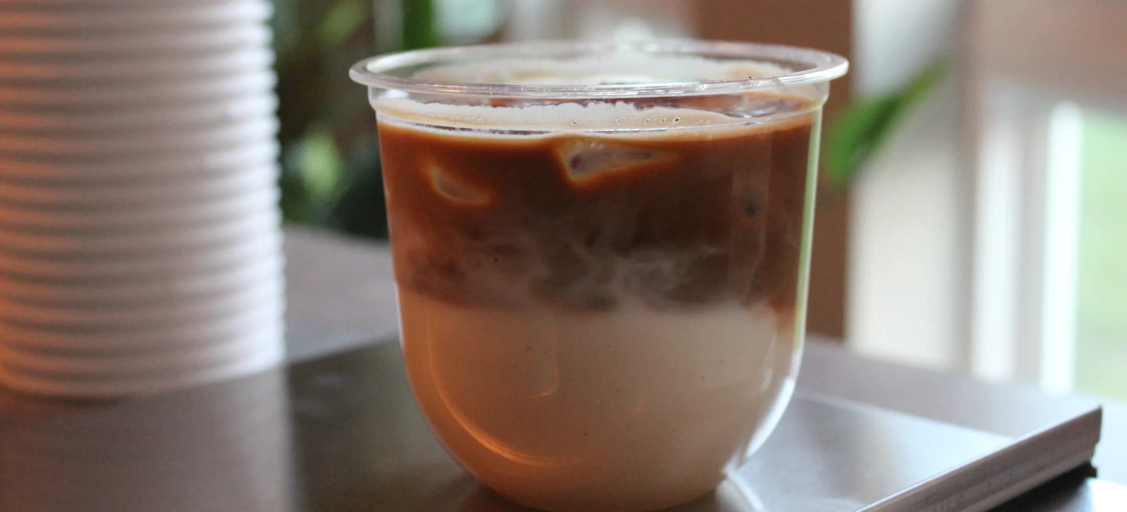 A layered iced latte on the cart counter, cups and greenery behind it