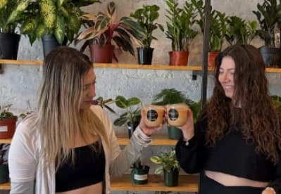 Two guests toasting branded Wooden Cow Coffee iced lattes in a plant-filled studio