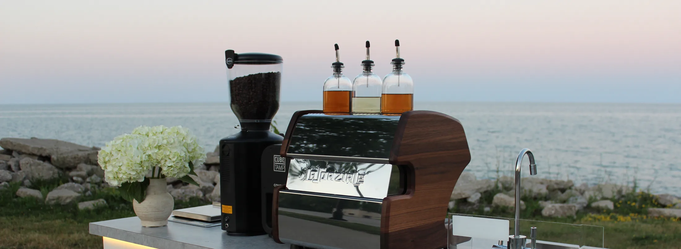 White hydrangeas and the espresso setup on the cart counter at a lakefront event in evening light